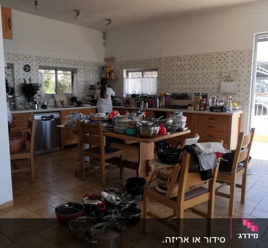 מטבח עם כלים וסירים על השולחן והרצפה, אישה מסדרת